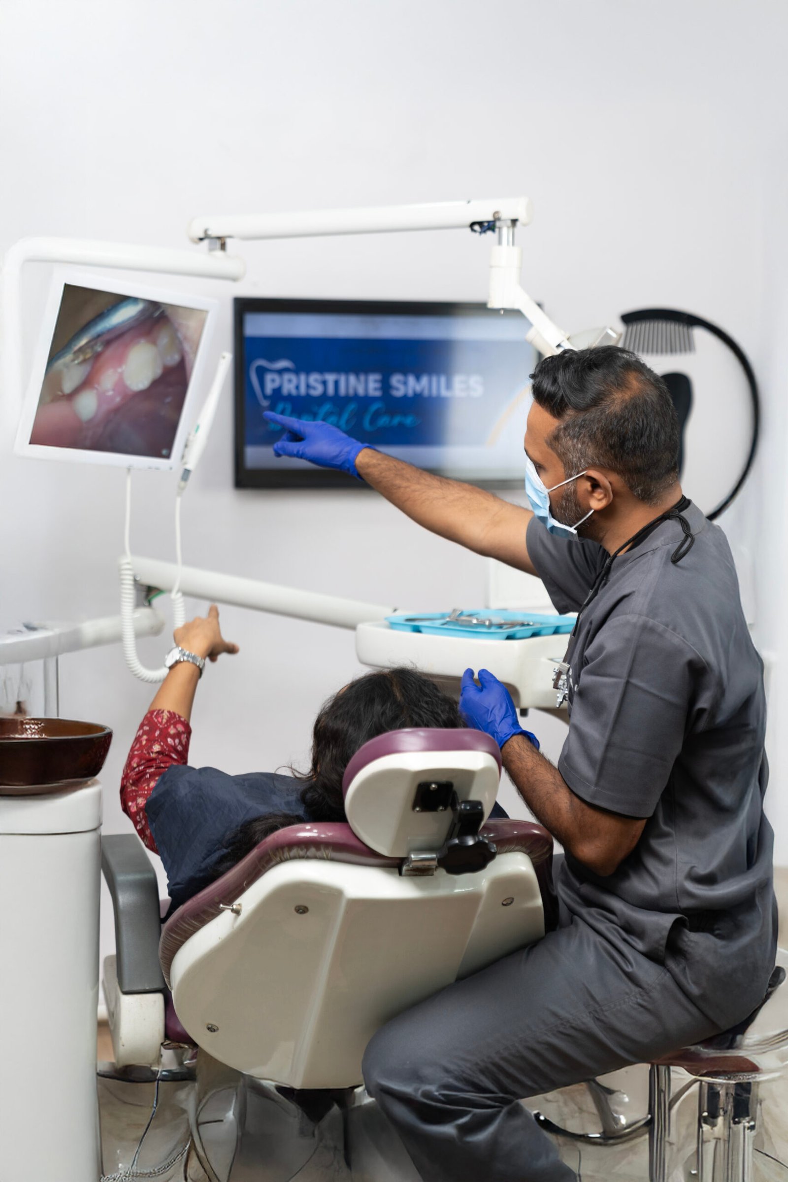 Dr. Sagar Lokhande, wearing a mask and explaining dental care to a patient in a clinical setting.